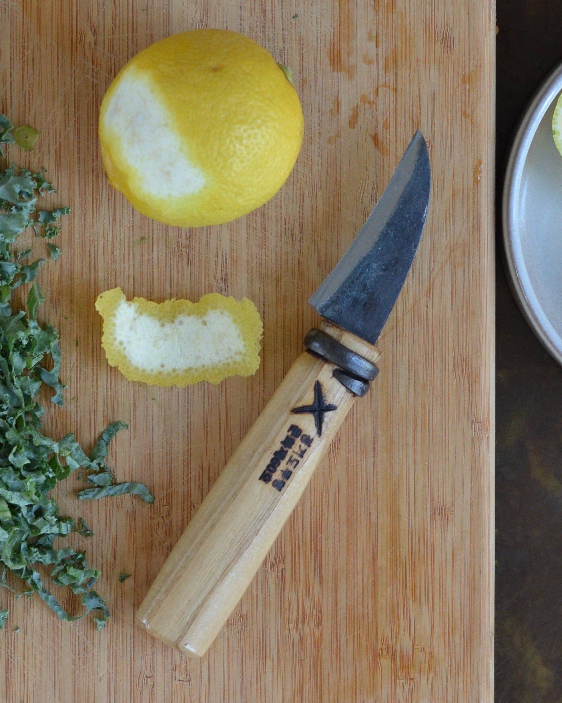 Knife with a wooden handle on a cutting board next to a lemon and herbs