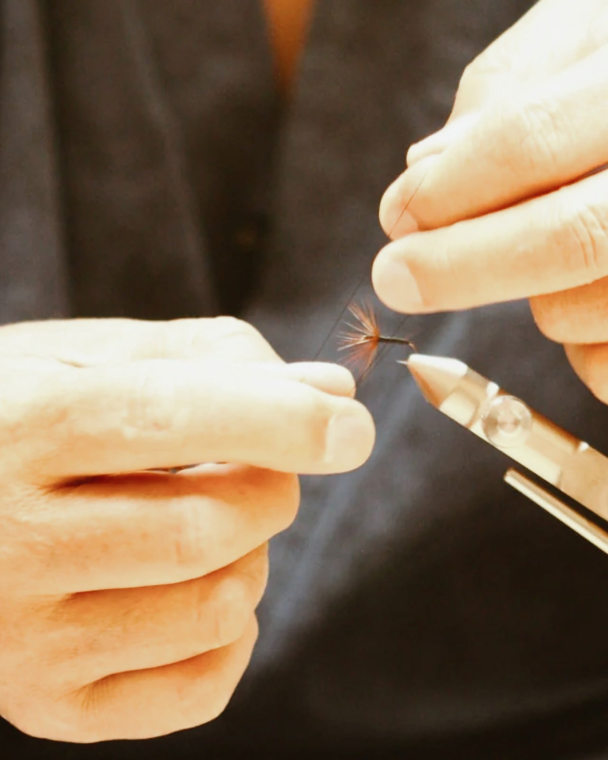 Close-up of hands using tweezers to handle a small object against a dark background